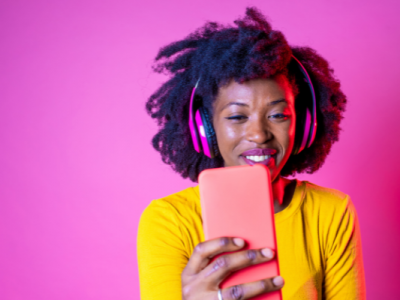 A guide to YouTube's algorithm 2023 - woman with headphones and phone in front of a pink background